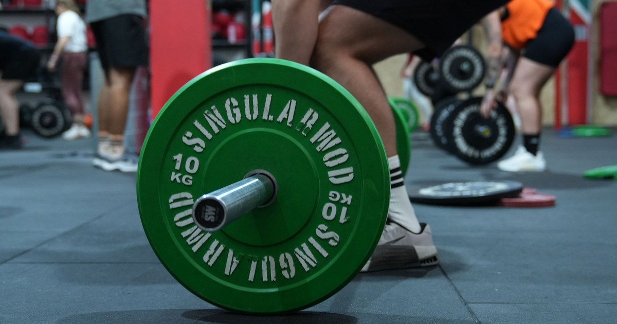 Atleta cargando una barra con discos verdes durante un WOD